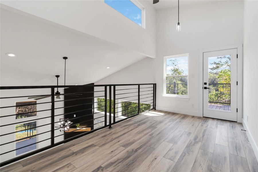 Versatile loft space ideal for a second living area, home office, or creative studio, featuring a ceiling fan, three pendant lights, and a door that opens to the upper balcony. Versatile loft space ideal for a second living area, home office, or creative studio, featuring a ceiling fan, three pendant lights, and a door that opens to the upper balcony.