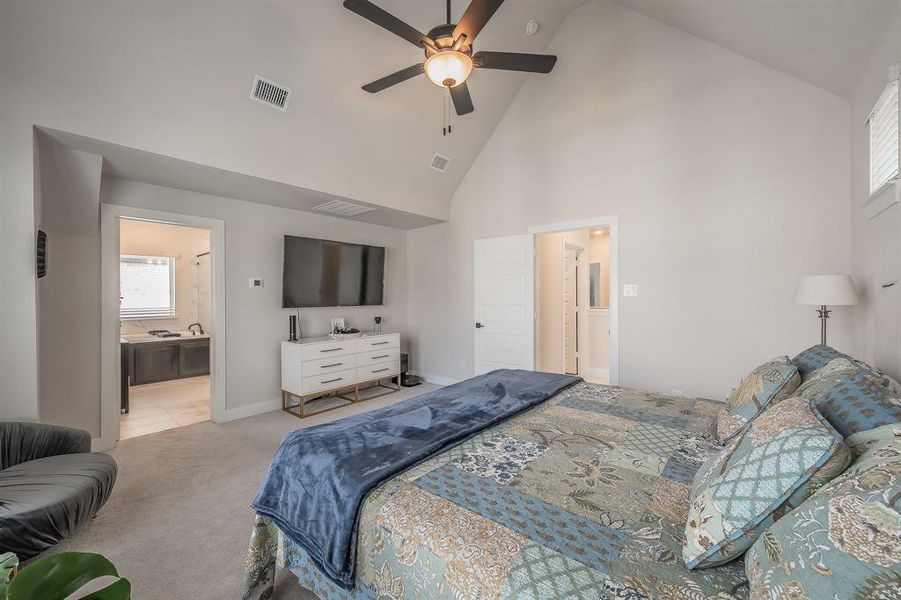 Carpeted bedroom featuring high vaulted ceiling, a ceiling fan, and ensuite bath