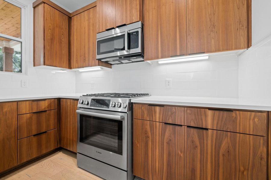 Kitchen with appliances with stainless steel finishes, modern cabinets, brown cabinets, and light countertops Kitchen with appliances with stainless steel finishes, modern cabinets, brown cabinets, and light countertops