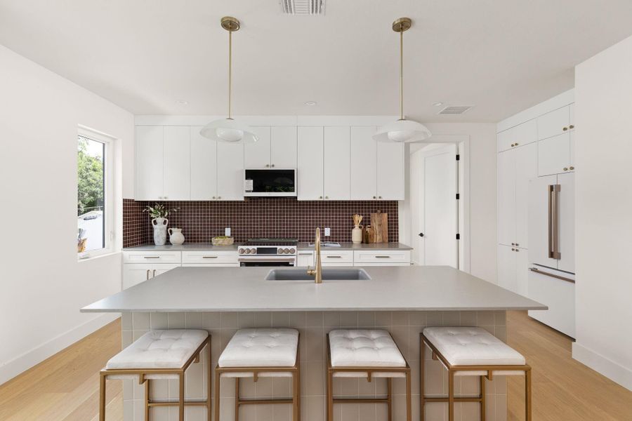 A well-lit kitchen with a spacious island, contemporary pendant lighting, and light wood flooring. A well-lit kitchen with a spacious island, contemporary pendant lighting, and light wood flooring.