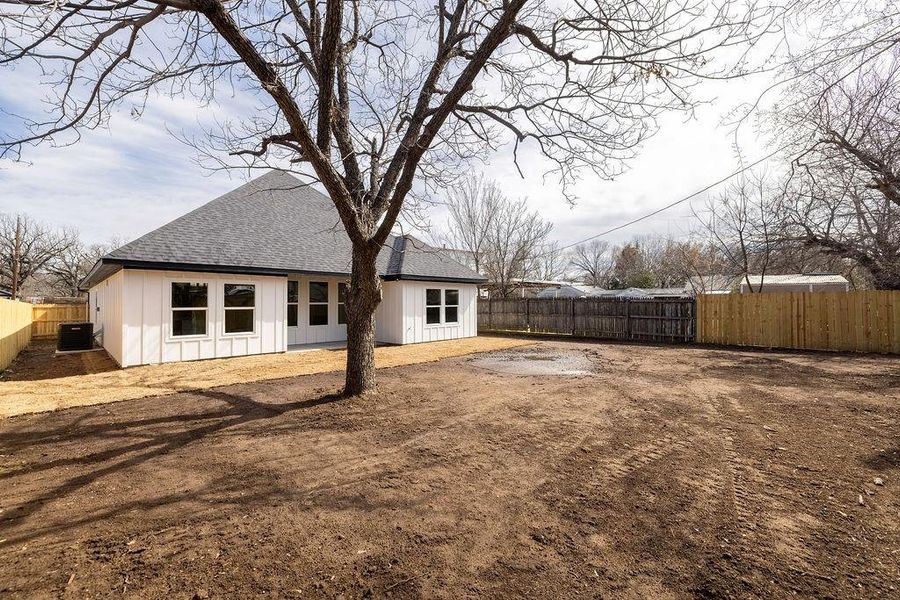 Back of house with central AC, board and batten siding, a fenced backyard, and roof with shingles