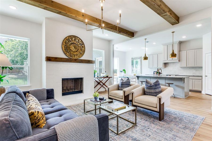 Living room featuring a brick fireplace, beamed ceiling, light wood-type flooring, and a wealth of natural light