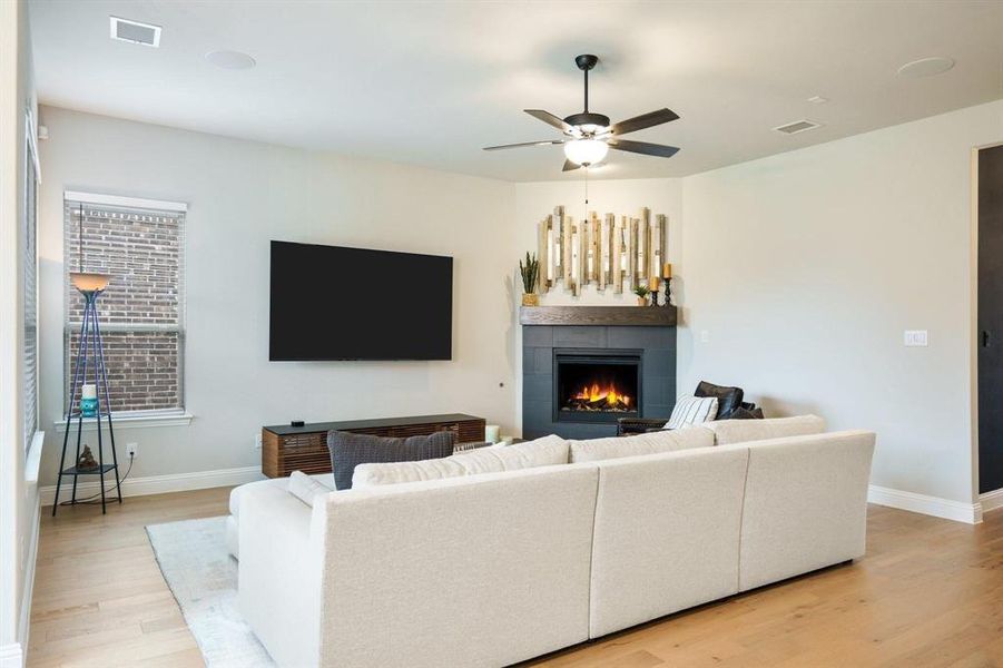 Living area featuring light wood-style flooring, a tile fireplace, and a ceiling fan Living area featuring light wood-style flooring, a tile fireplace, and a ceiling fan