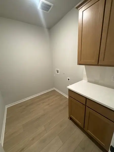 Dedicated utility area featuring wood-finish flooring, light tan cabinetry, and a white countertop