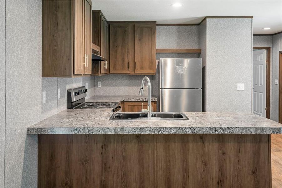 Kitchen with appliances with stainless steel finishes, a peninsula, light countertops, and under cabinet range hood