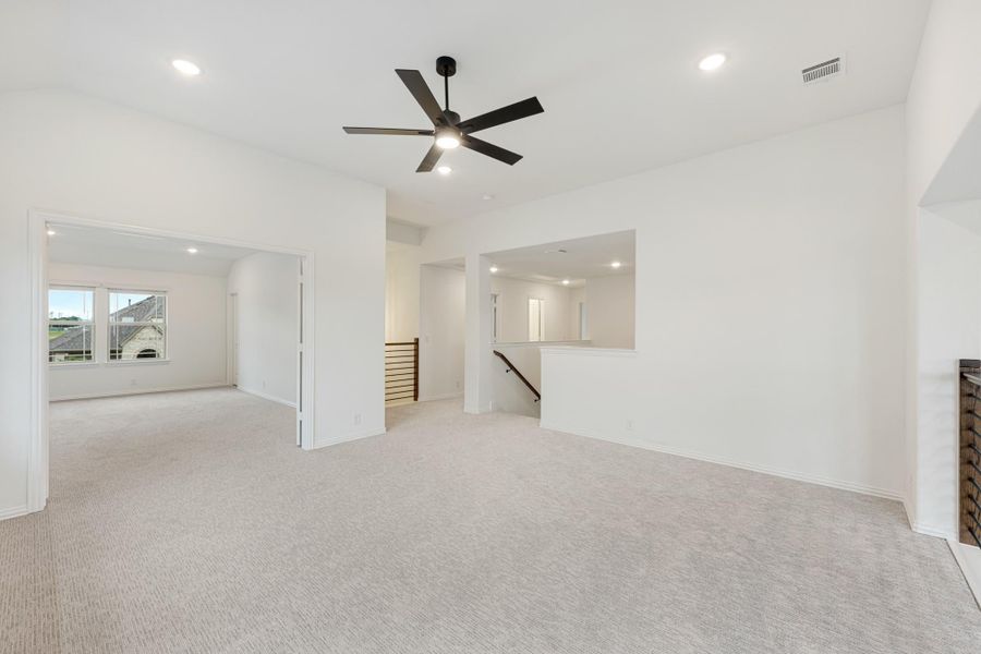 Open upstairs living area with carpet, black ceiling fan, and staircase landing nearby Open upstairs living area with carpet, black ceiling fan, and staircase landing nearby