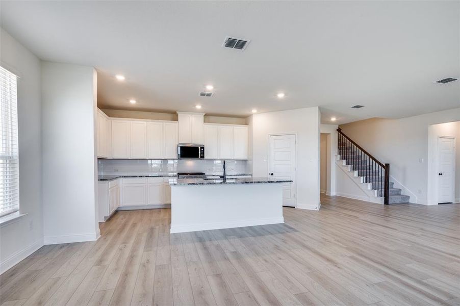 Kitchen featuring decorative backsplash, light wood finished floors, an island with sink, dark stone countertops, and stainless steel microwave Kitchen featuring decorative backsplash, light wood finished floors, an island with sink, dark stone countertops, and stainless steel microwave