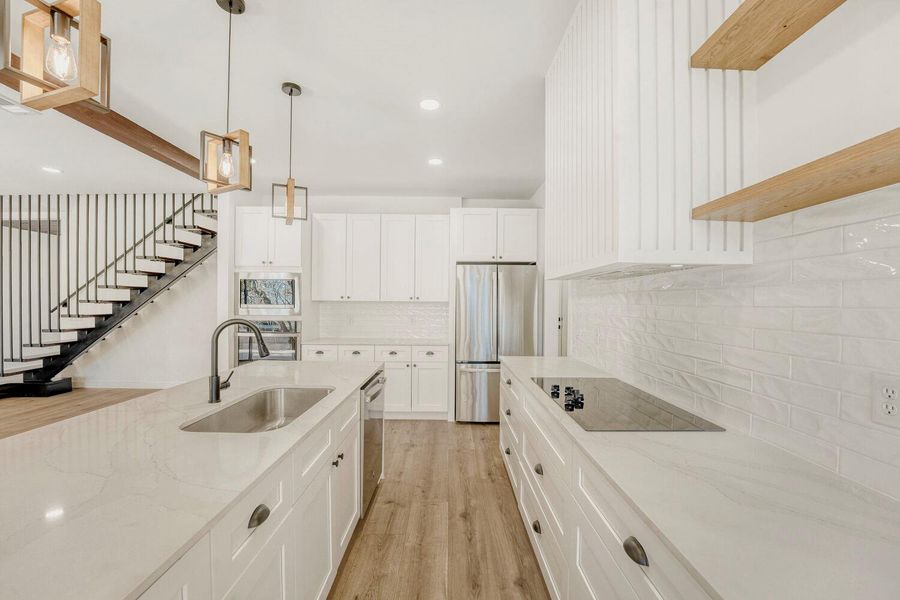 Kitchen with stainless steel appliances, white cabinetry, light stone countertops, and light wood finished floors