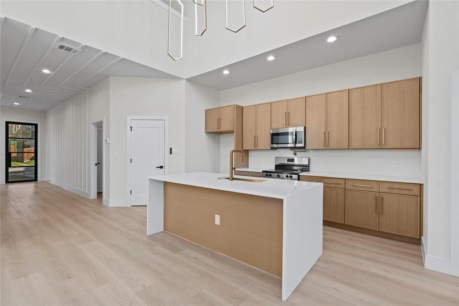 Kitchen with light countertops, light wood-style flooring, appliances with stainless steel finishes, a sink, and an island with sink