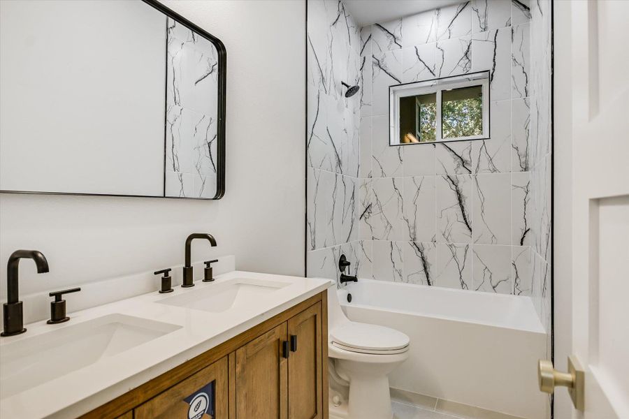 A well-appointed bathroom featuring a double vanity, elegant black fixtures, and striking marble-patterned tile work around the bath and shower.
