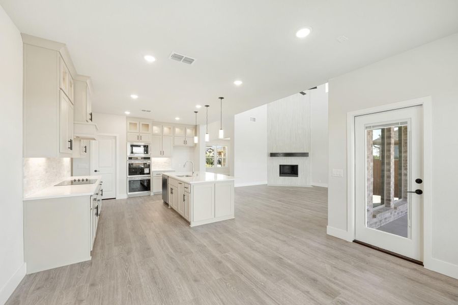 Open-concept kitchen with white cabinets, center island, stainless appliances, and light wood floors opening to living area with fireplace.