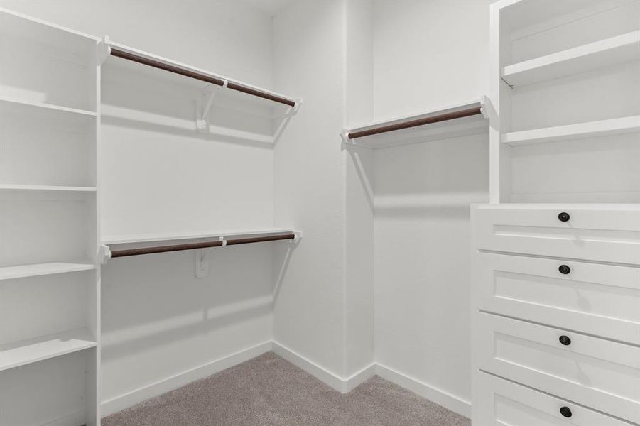 This is a spacious, well-organized walk-in closet featuring multiple shelves and hanging rods, complemented by a built-in white dresser for additional storage.