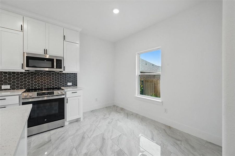 Kitchen with appliances with stainless steel finishes, light countertops, white cabinetry, backsplash, and light marble finish floors