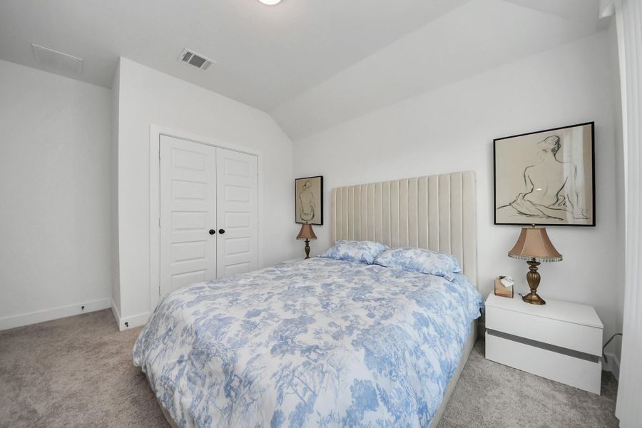 This bedroom features a comfortable bed with a patterned blue and white comforter, flanked by modern white nightstands and elegant lamps. The room has clean white walls, a double-door closet, and artwork above the headboard, creating a cozy and inviting atmosphere. This bedroom features a comfortable bed with a patterned blue and white comforter, flanked by modern white nightstands and elegant lamps. The room has clean white walls, a double-door closet, and artwork above the headboard, creating a cozy and inviting atmosphere.