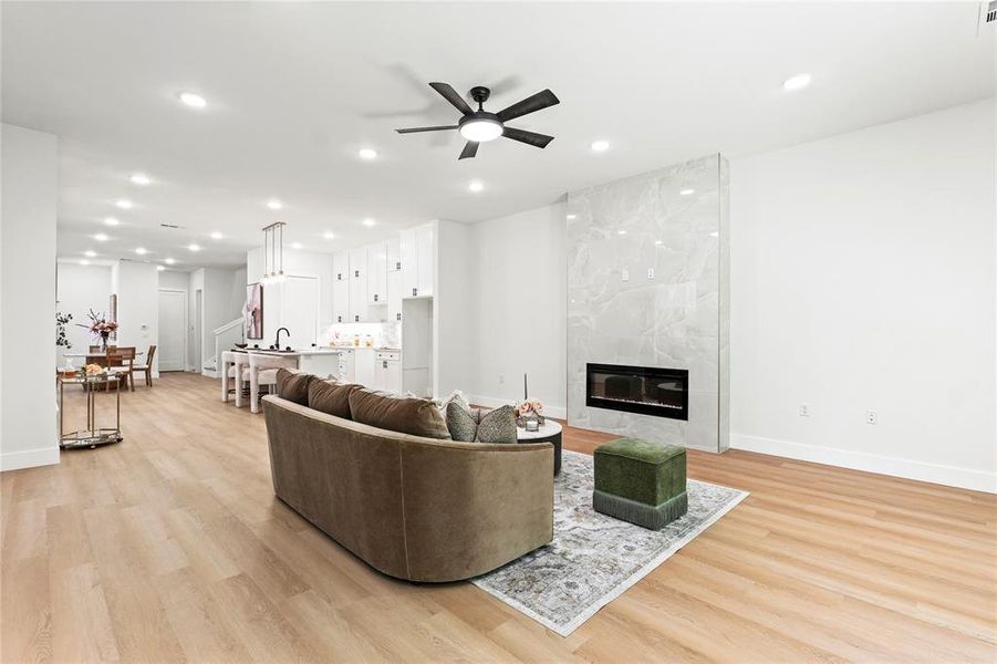 Living room featuring light wood-style floors, ceiling fan, a high end fireplace, and recessed lighting Living room featuring light wood-style floors, ceiling fan, a high end fireplace, and recessed lighting
