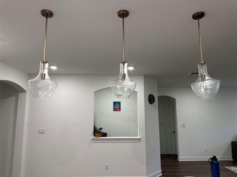 Three clear glass pendant lights with brass-finish accents illuminate the interior space, featuring a wall niche and arched doorways Three clear glass pendant lights with brass-finish accents illuminate the interior space, featuring a wall niche and arched doorways