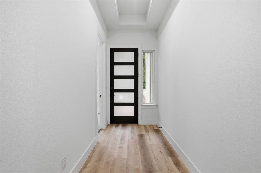 Entryway featuring a contemporary black door with five frosted glass lites, a vertical sidelight window with white blinds, and wood-finish flooring