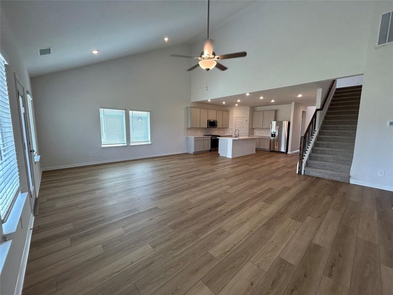 Unfurnished living room with light wood-type flooring, high vaulted ceiling, ceiling fan, recessed lighting, and stairs Unfurnished living room with light wood-type flooring, high vaulted ceiling, ceiling fan, recessed lighting, and stairs