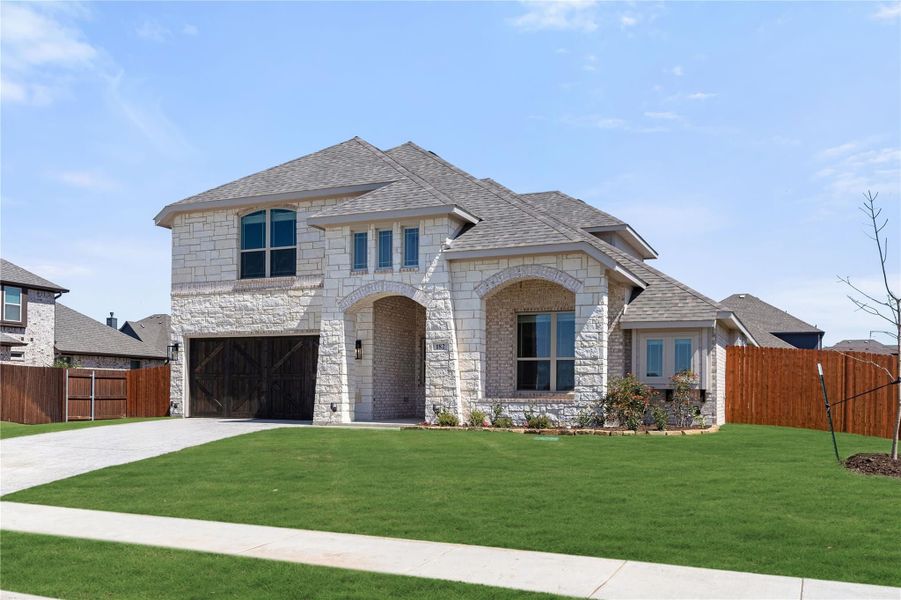 Two-story home with light stone exterior, two-car garage, arched entry, and green front lawn