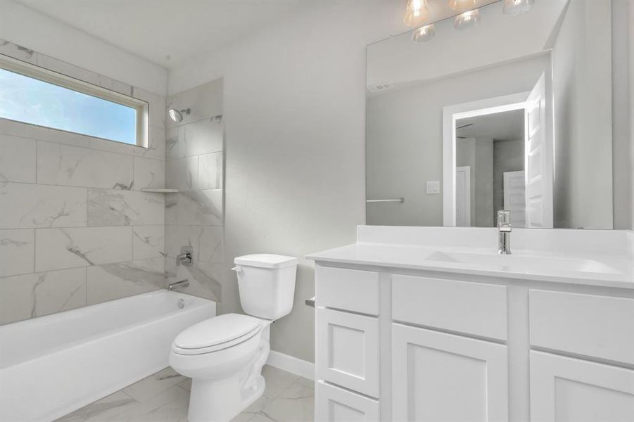 Secondary bathroom. Bath/shower combo with tile surround, light wood cabinets complete with a beautiful light countertop, this bathroom combines style and functionality for a truly inviting ambiance. Sample photo of completed home with similar floor plan. As-built interior colors and selections may vary.