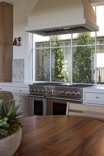 Kitchen with custom exhaust hood, plenty of natural light, light stone counters, and range with two ovens Kitchen with custom exhaust hood, plenty of natural light, light stone counters, and range with two ovens