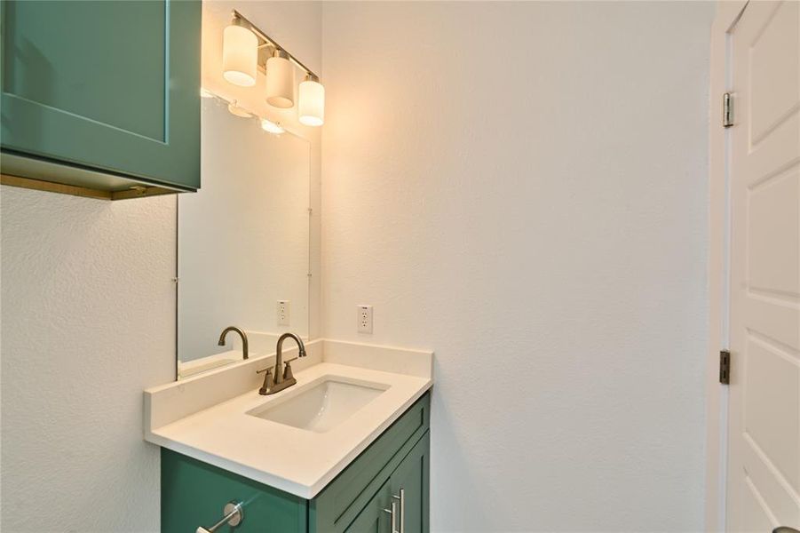 Bathroom vanity featuring teal cabinetry, a white countertop, an integrated sink, and a bronze-finish faucet