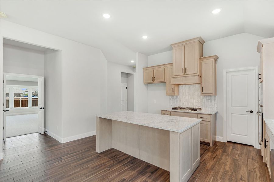 Kitchen with center island, granite countertops, light wood cabinets, tile backsplash, and dark hardwood floors Kitchen with center island, granite countertops, light wood cabinets, tile backsplash, and dark hardwood floors