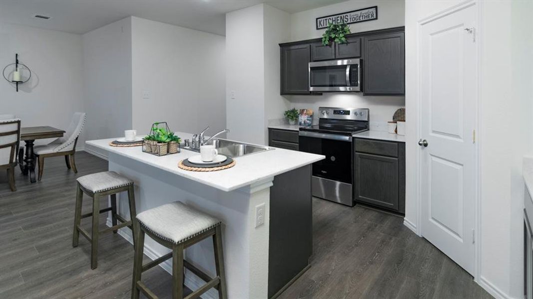 Kitchen featuring stainless steel appliances, a kitchen breakfast bar, a kitchen island with sink, and dark wood-style floors