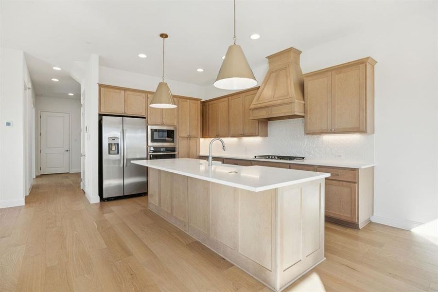 Kitchen with light brown cabinetry, stainless steel appliances, pendant lighting, light wood-style flooring, and recessed lighting