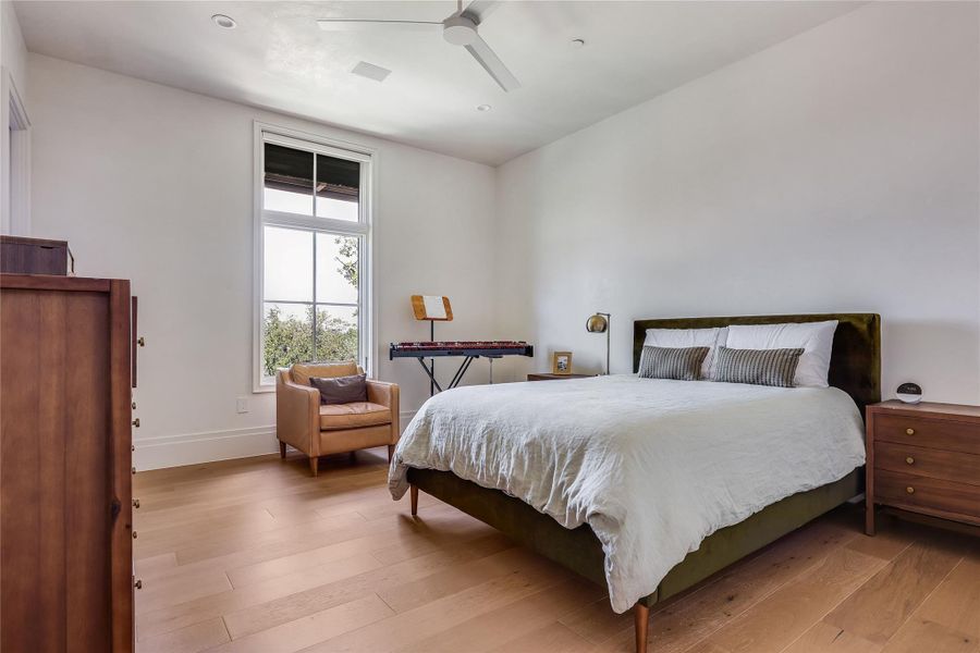 Naturally illuminated bedroom with wide-plank hardwood flooring and a ceiling fan.