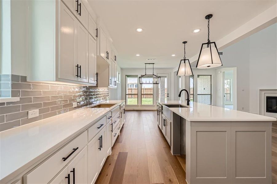 Kitchen with light wood-type flooring, white cabinets, a kitchen island with sink, pendant lighting, and sink