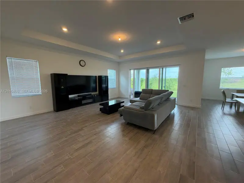 Tray ceiling with recessed lighting, wood-finish tile flooring, and sliding glass doors providing outdoor access