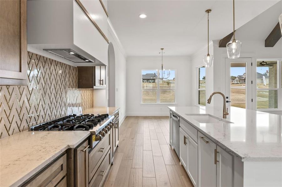 Gourmet kitchen featuring a professional-grade gas range, custom chevron-patterned tile backsplash, and light-toned countertops