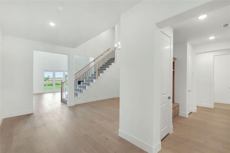 Open foyer with light wood floors, white walls, and staircase with black metal balusters and wood handrail