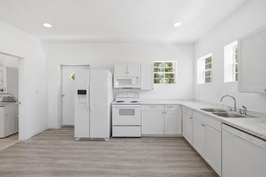 Bright kitchen featuring white cabinetry, light countertops, and white appliances including a refrigerator, range, microwave, and dishwasher