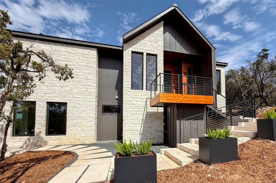 Modern home featuring stone siding, a balcony, board and batten siding, and stairs