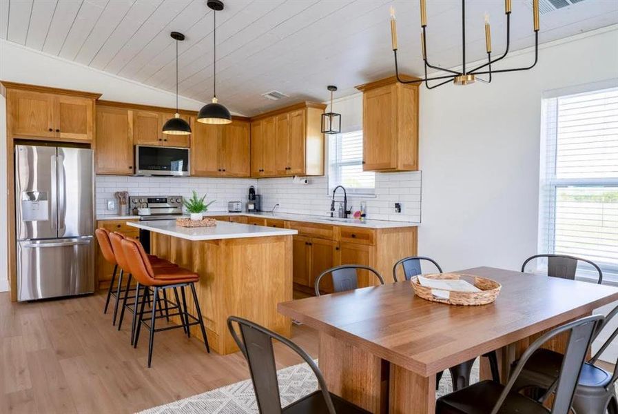 This kitchen features wood cabinetry, stainless steel appliances, and a central island with seating