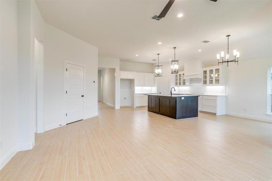 Kitchen featuring white cabinets, sink, light hardwood / wood-style flooring, a center island with sink, and backsplash