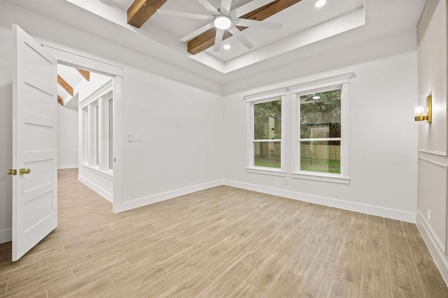 Spacious room featuring wood-finish tile flooring, a tray ceiling with exposed wood beams, and recessed lighting