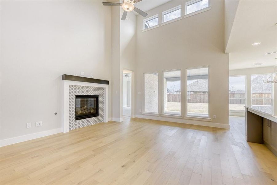 Unfurnished living room with ceiling fan, a tile fireplace, light wood-style floors, and a high ceiling