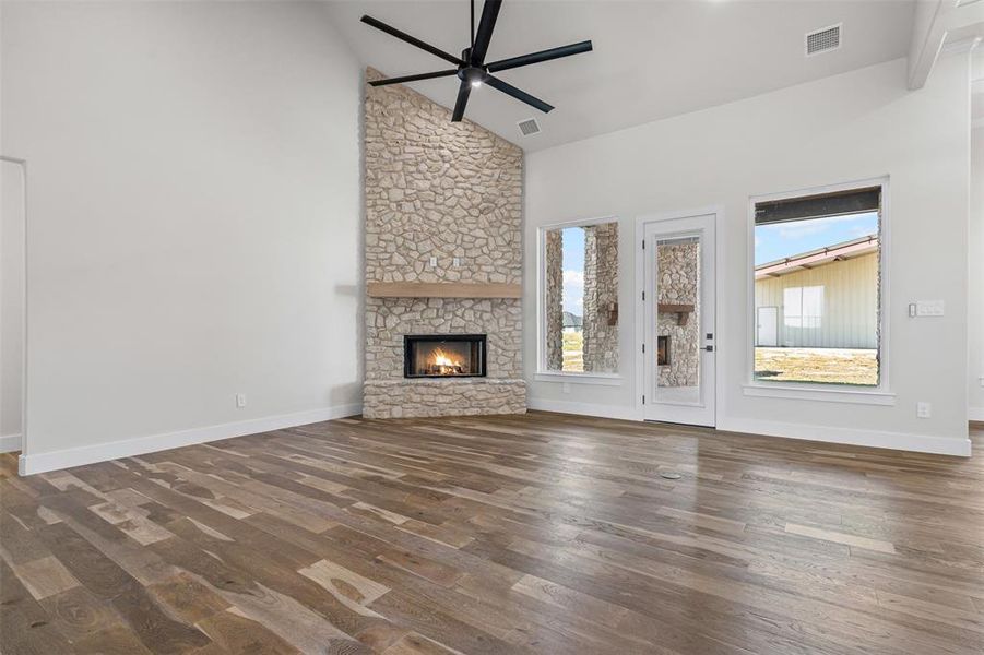 Unfurnished living room featuring high vaulted ceiling, a stone fireplace, dark wood-style flooring, and a ceiling fan