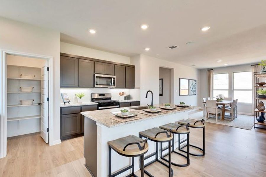 Kitchen with light stone counters, a kitchen island with sink, stainless steel appliances, a sink, and light wood-style floors