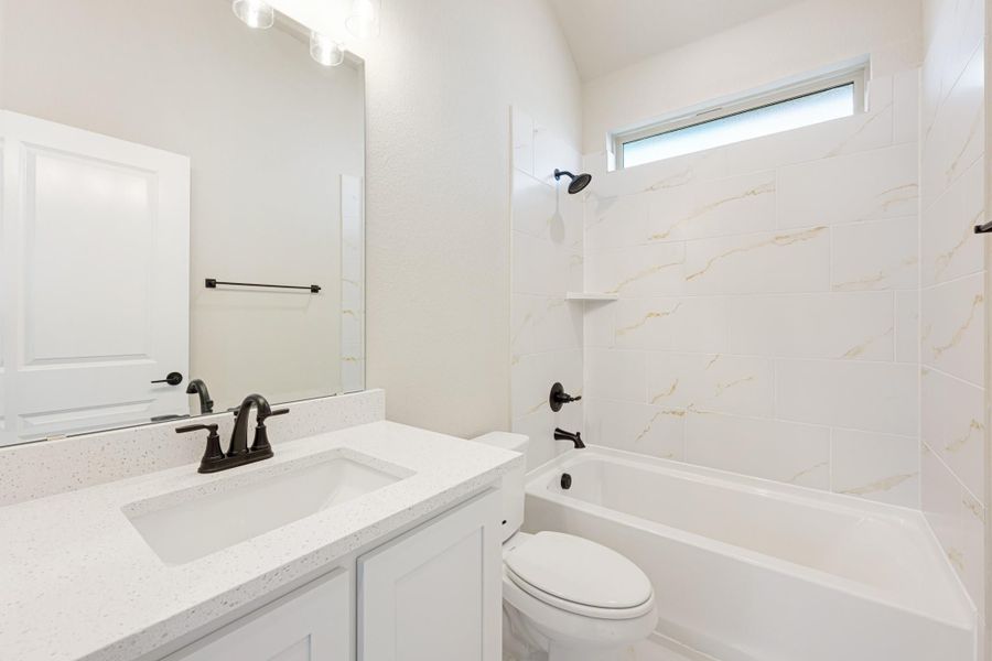 White bathroom with quartz vanity, tub-shower combo with marble tile surround, and dark bronze fixtures
