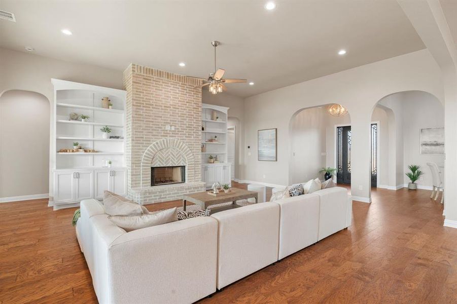 Living room featuring a brick fireplace, ceiling fan, hardwood / wood-style flooring, and built in features