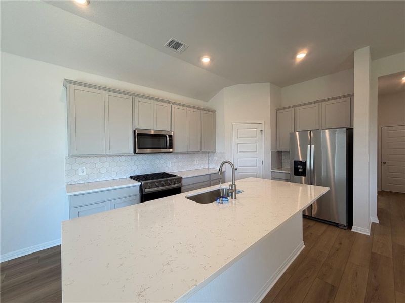 Kitchen with tasteful backsplash, appliances with stainless steel finishes, light stone counters, dark wood-style floors, and lofted ceiling Kitchen with tasteful backsplash, appliances with stainless steel finishes, light stone counters, dark wood-style floors, and lofted ceiling