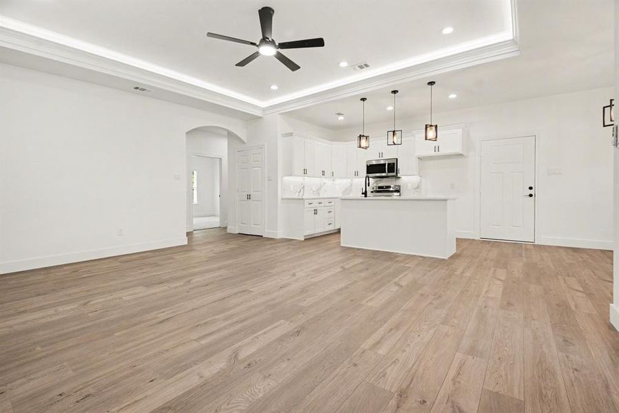 Open concept living space featuring light wood-look flooring, a modern kitchen with white cabinetry and stainless steel appliances, and recessed lighting in the ceiling