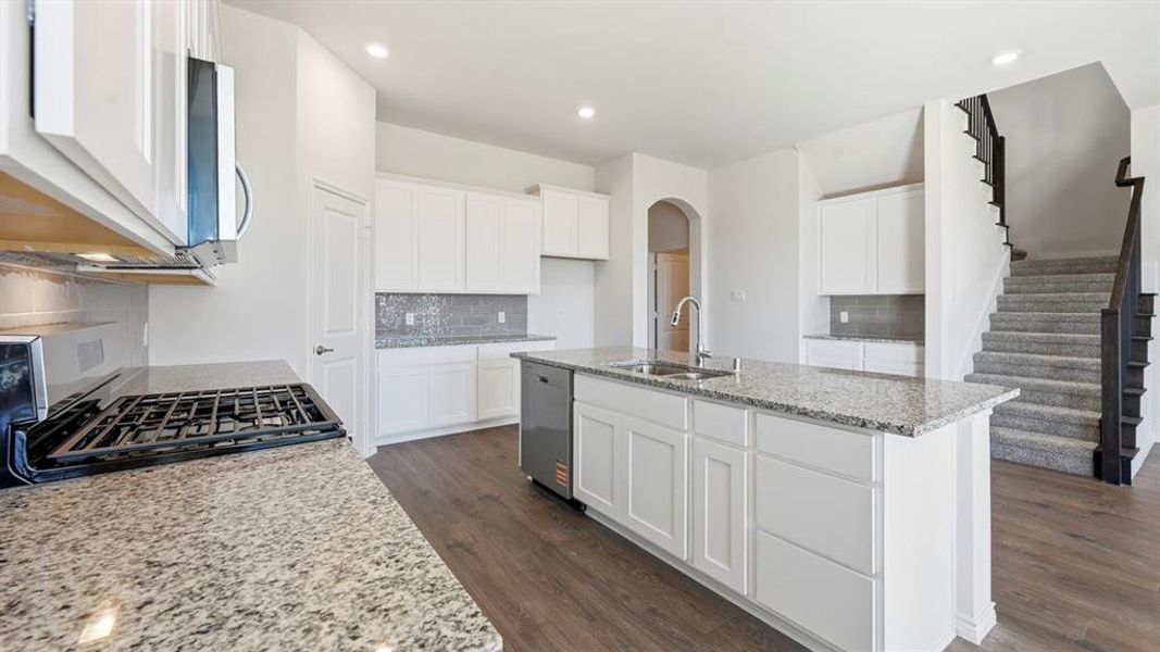 Kitchen with light stone counters, arched walkways, white cabinetry, an island with sink, and recessed lighting Kitchen with light stone counters, arched walkways, white cabinetry, an island with sink, and recessed lighting