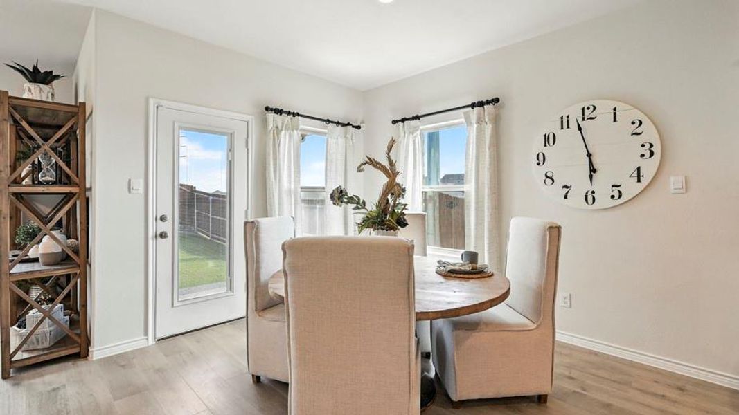 The dining area features light-colored flooring, a glass-paneled door, and windows with white curtains, providing views of the outdoor space