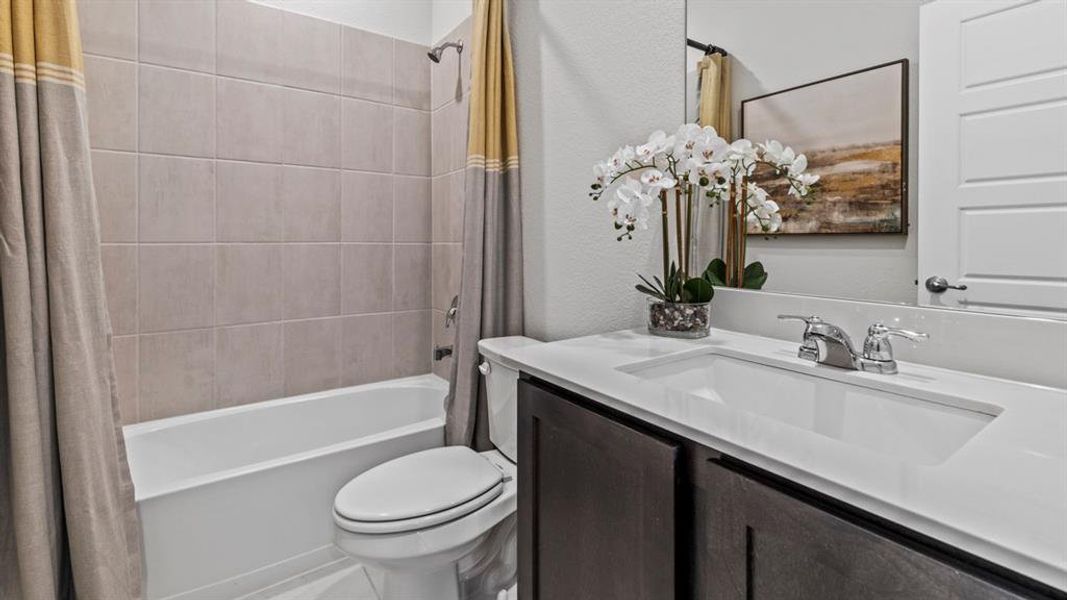Bathroom featuring a built-in bathtub with subway tile surround, white toilet, dark wood-finish vanity with integrated sink, and chrome fixtures Bathroom featuring a built-in bathtub with subway tile surround, white toilet, dark wood-finish vanity with integrated sink, and chrome fixtures