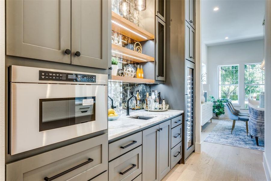 Bar with gray cabinetry, tasteful backsplash, light hardwood / wood-style flooring, sink, and light stone countertops